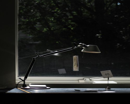 A desk lamp casting soft warm light over an open book next to a window