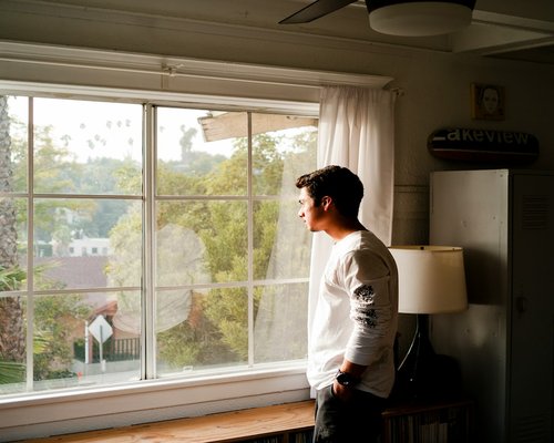 Person resting eyes by looking out of a window with soft daylight